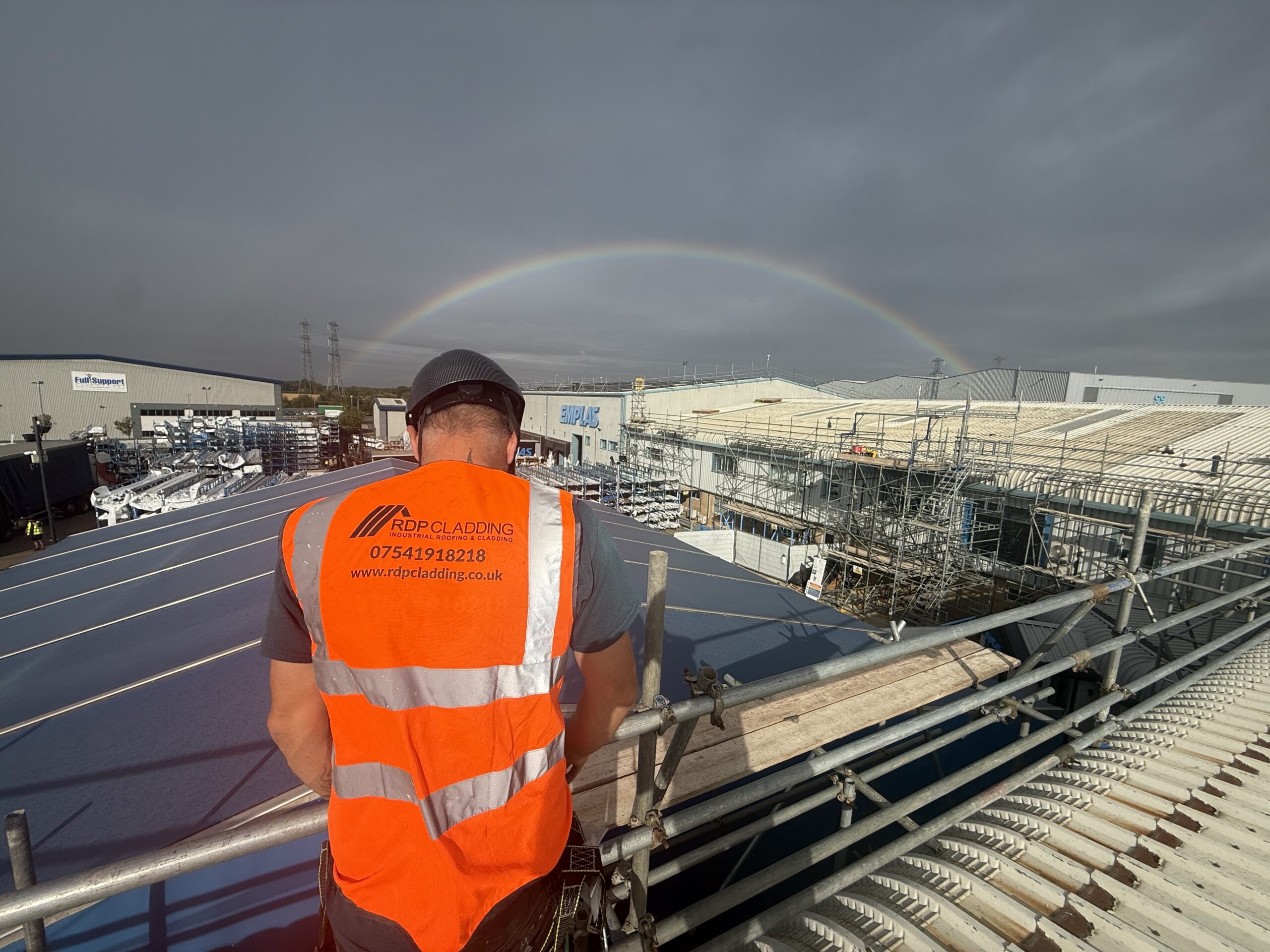 IMG_6118 RDP Cladding engineer overlooking the Emplas Windows factory roof refurbishment in Wellingborough, with scaffolding in place and a rainbow arching over the site during installation of the new solar-ready roofing system.