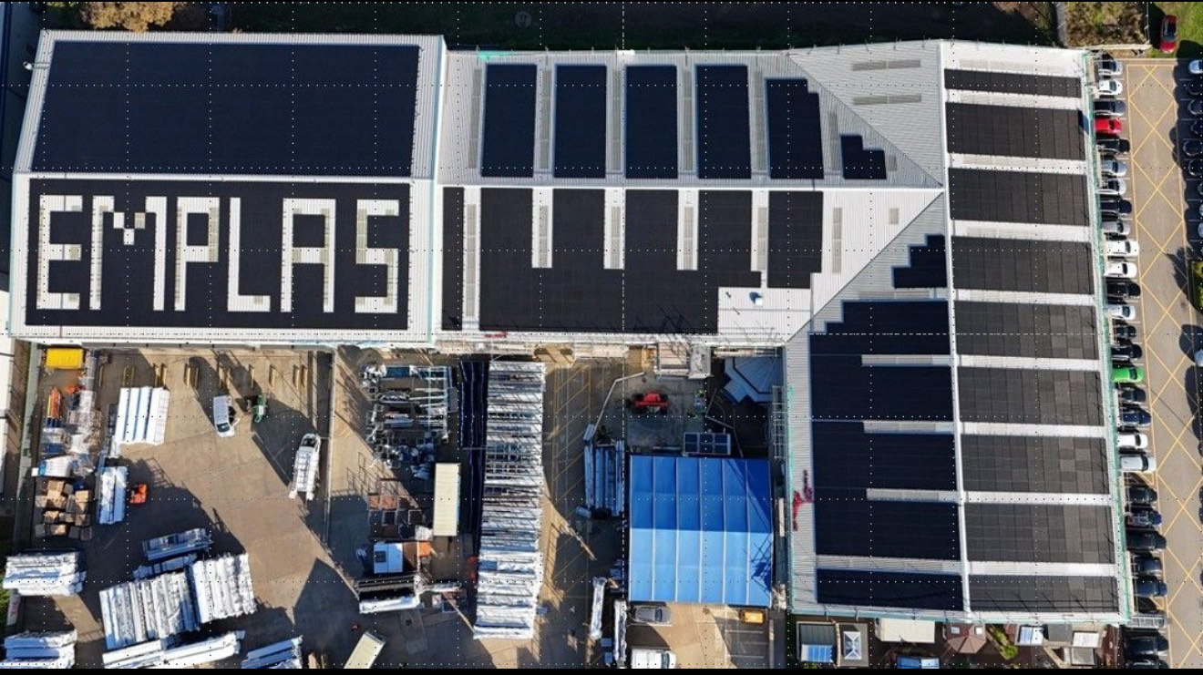 Aerial view of Emplas Windows’ Wellingborough manufacturing facility featuring a large-scale solar PV installation by RDP Cladding and Green Revolution Ltd, with solar panels arranged to spell “EMPLAS” across the new metal roof system.