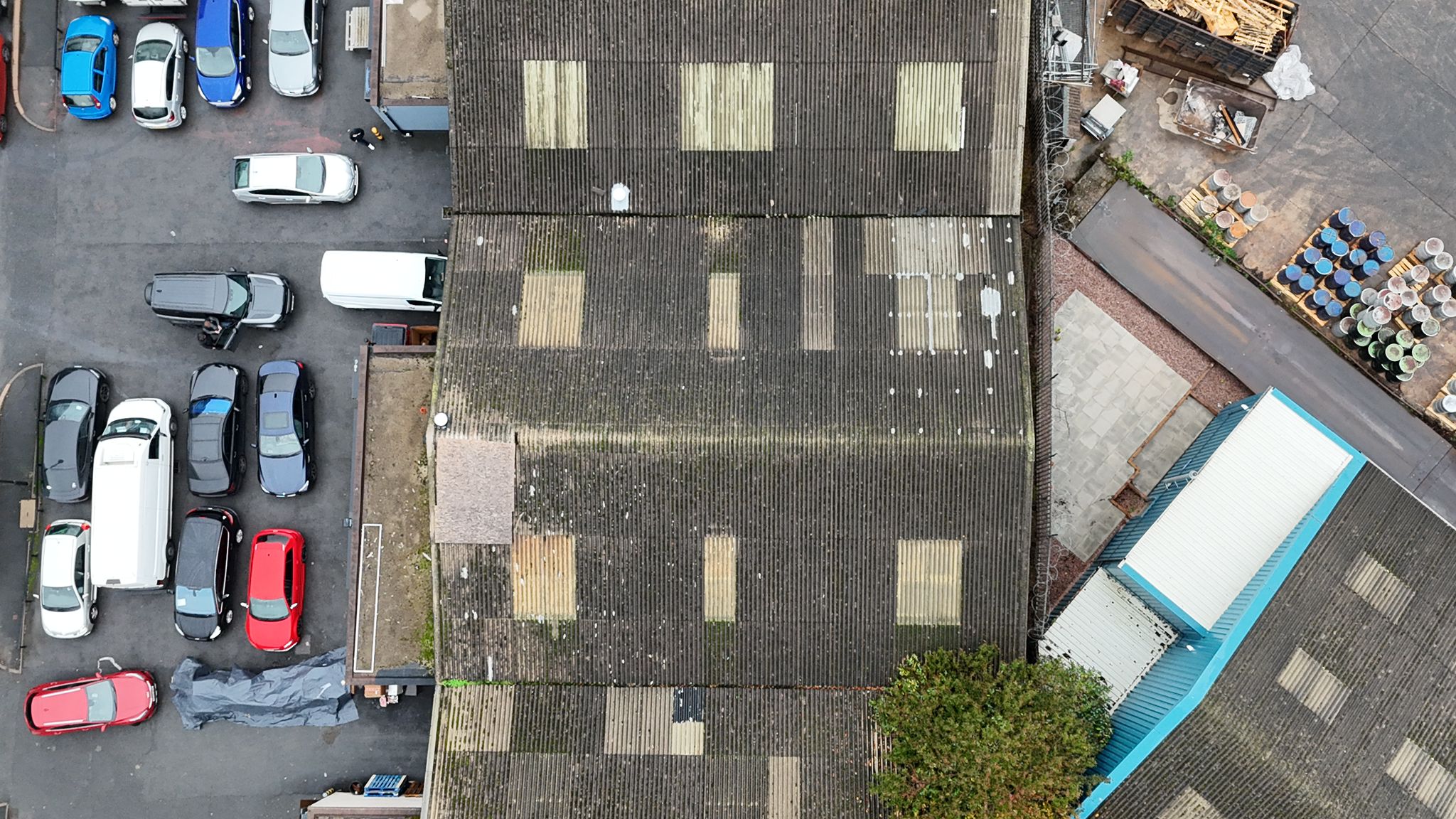 WhatsApp Image 2026-02-17 at 19.53.55 Aerial drone survey showing deteriorated asbestos cement roof with multiple patch repairs across a commercial garage building prior to full strip and replacement