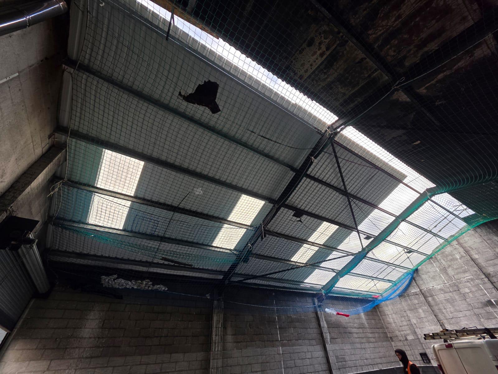 WhatsApp Image 2026-02-17 at 19.57.48 (2) Interior view of a fire-damaged commercial building showing holes in the roof covering and safety netting installed beneath the roof structure prior to strip and replacement works