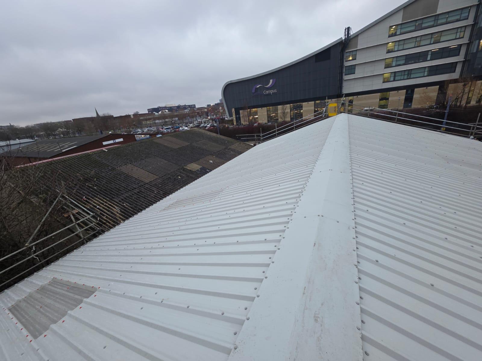 WhatsApp Image 2026-02-17 at 19.57.48 (4) Completed apex ridge of a new white profiled metal roof showing neat fastening detail, with a deteriorated asbestos cement roof visible on an adjacent building and scaffolding to the side