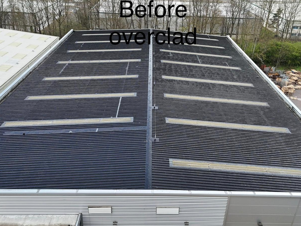 Aerial view of a dark industrial roof with multiple rooflight strips before overcladding works, labelled "Before overclad"