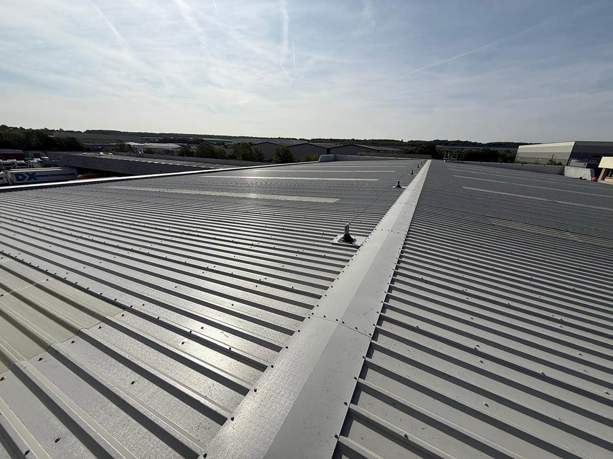 Completed grey profiled metal roof showing the ridge flashing running between two pitches, with a roof vent in the foreground