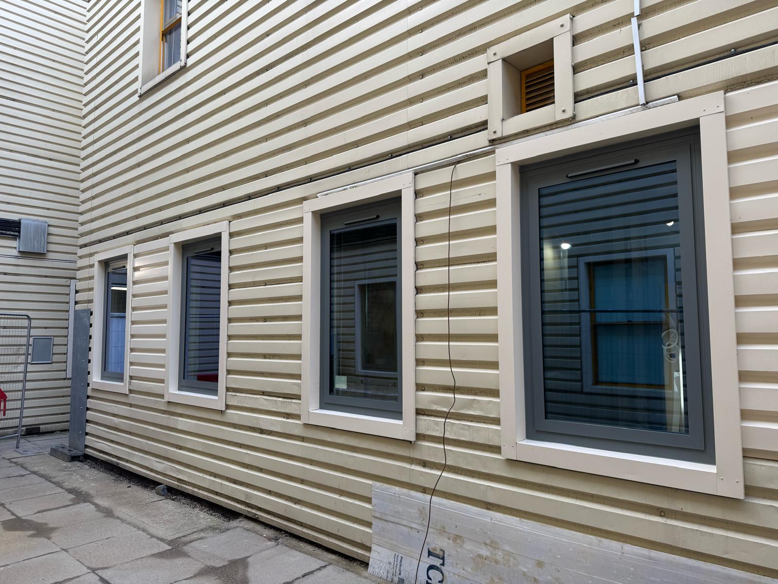 Completed wall cladding facade with four new window openings installed, finished with white flashings on a cream profiled metal cladding building